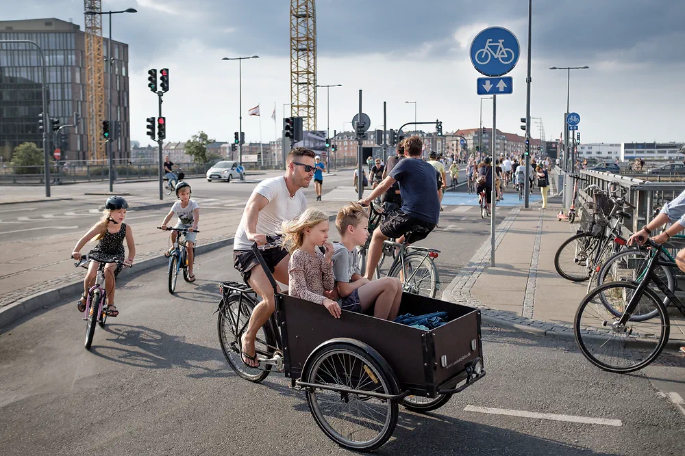 Father riding a cargo bike with his children in Copenhagen, two kids cycling alongside