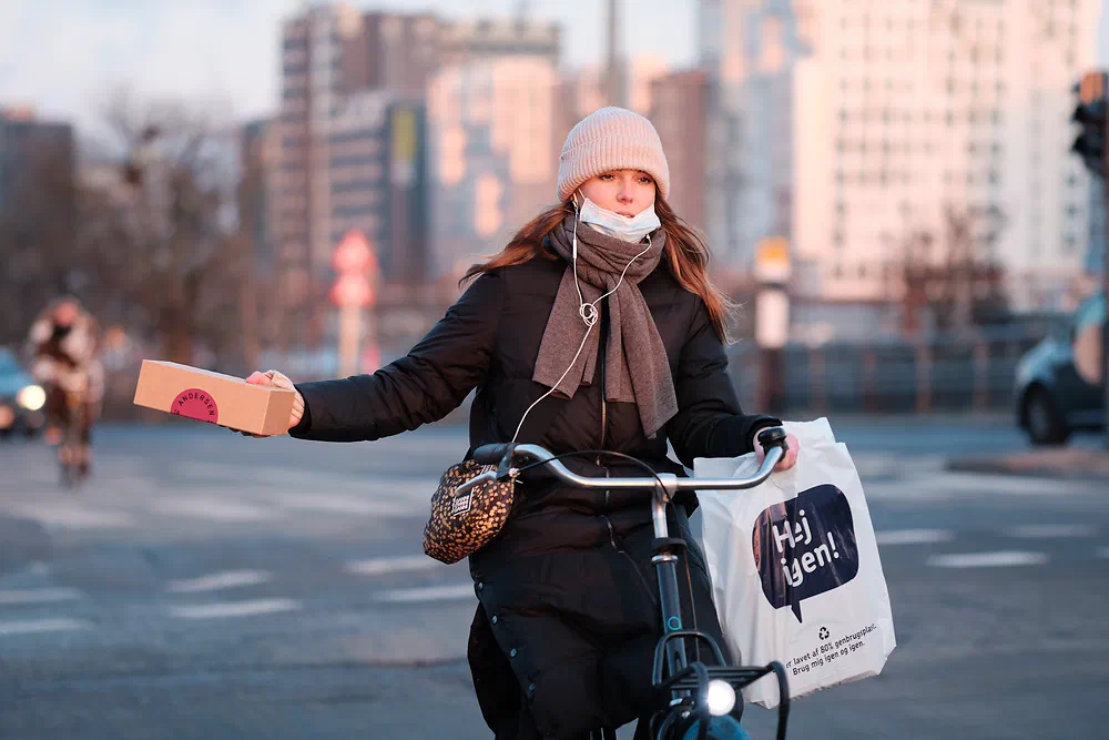 Woman in a pink hat holding out a parcel while cycling near Dybbølsbro