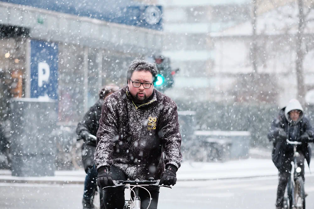 Bearded man cycling through falling snow in Copenhagen