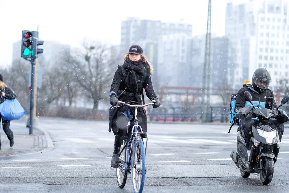Woman cycling in light snow next to a scooter rider
