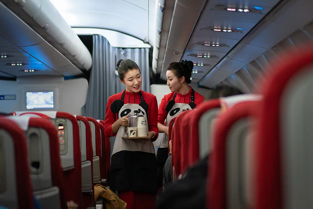 Two Sichuan Airlines flight attendants in panda aprons serving in the aisle