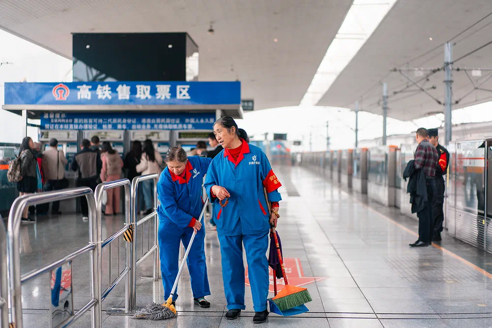 Two cleaners in blue uniforms mopping a station platform in Chengdu