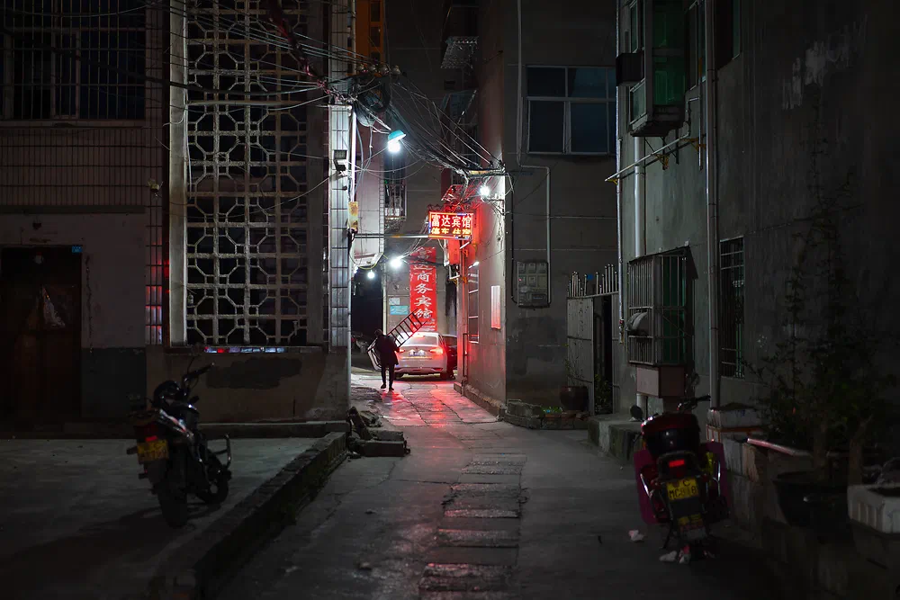 Narrow back alley at night with red lanterns and parked scooters in Yunxi
