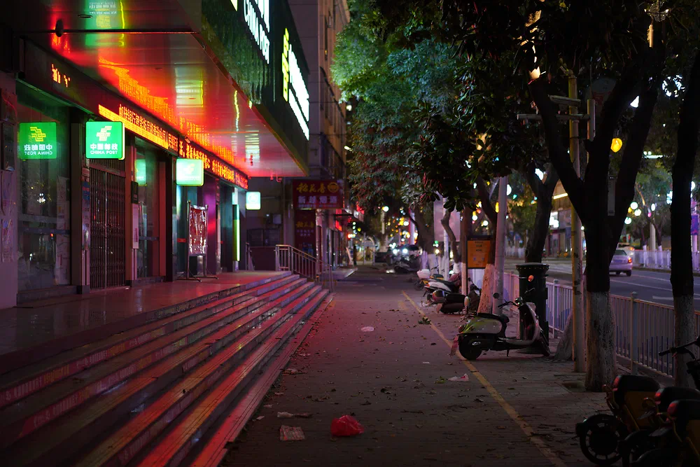 Wide empty steps and a street lit by neon shop signs at night in Yunxi