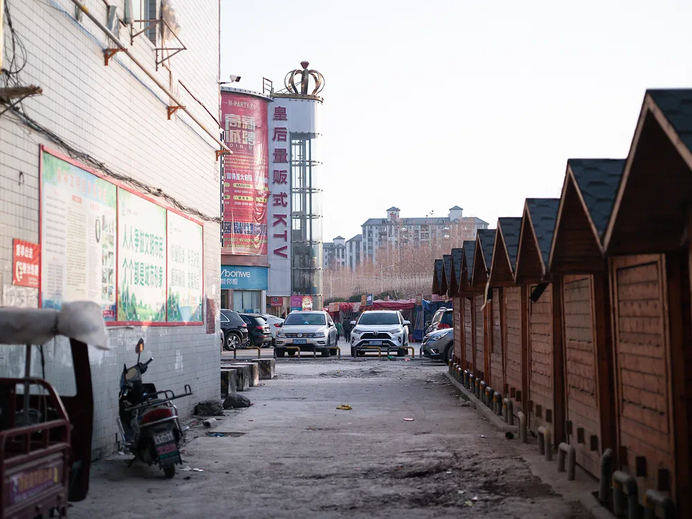 Row of wooden market stalls next to a shopping mall with a KTV sign in Yunxi