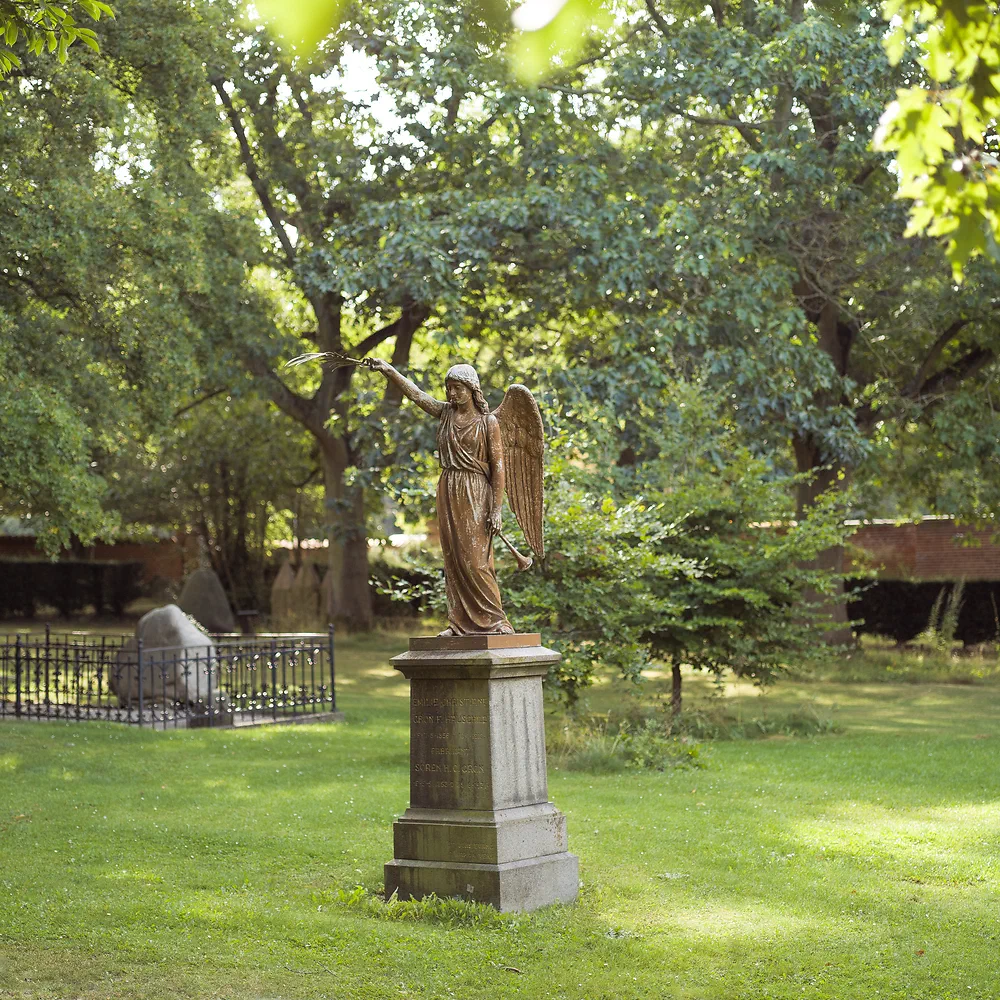 Angel statue on a tall pedestal in the sunny green Solbjerg Park Cemetery