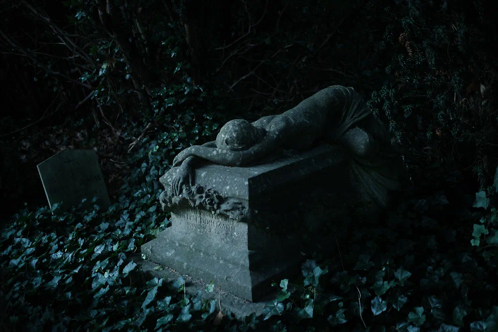 Statue of a grieving figure lying on a tomb surrounded by ivy at dusk