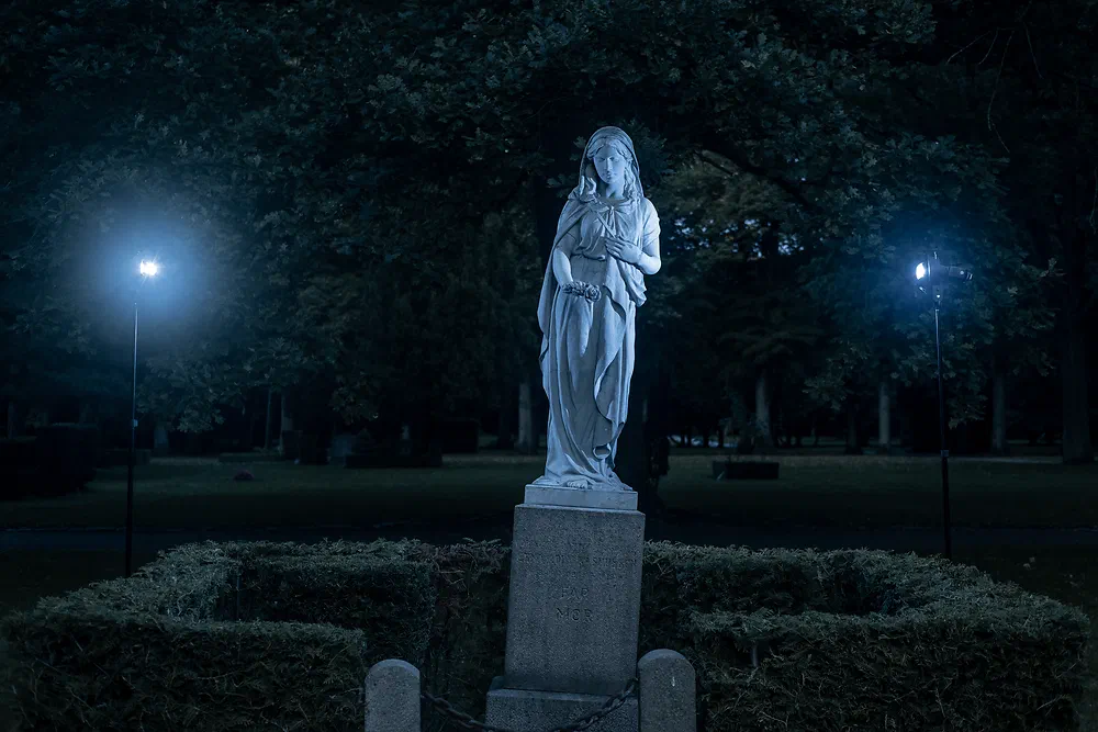 Statue at Vestre Kirkegård at night between two glowing lamps