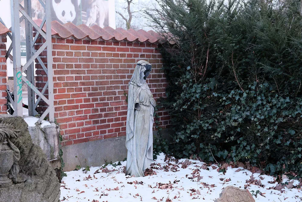Headless veiled statue by a red brick wall with snow on the ground at Solbjerg Park Cemetery