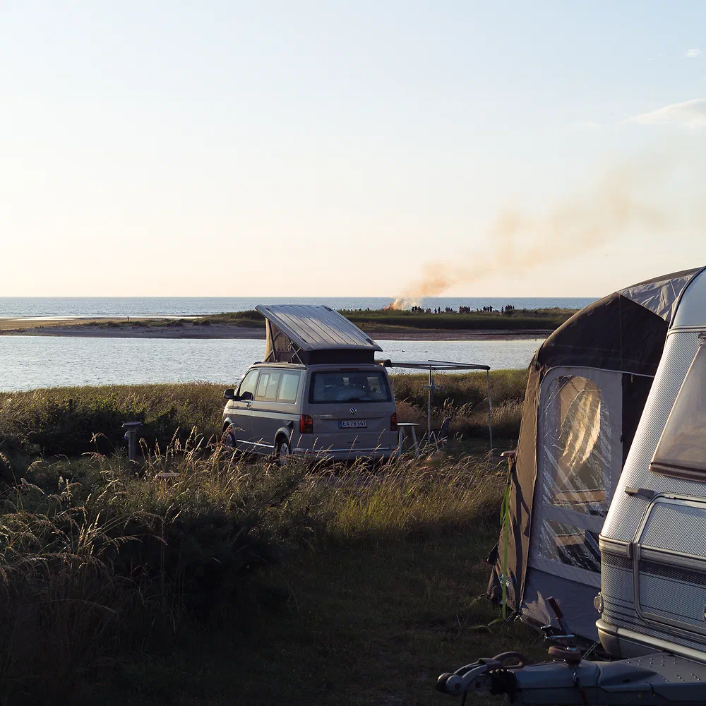 Camper van and caravan in the dunes by the water at sunset at Sanddobberne Camping