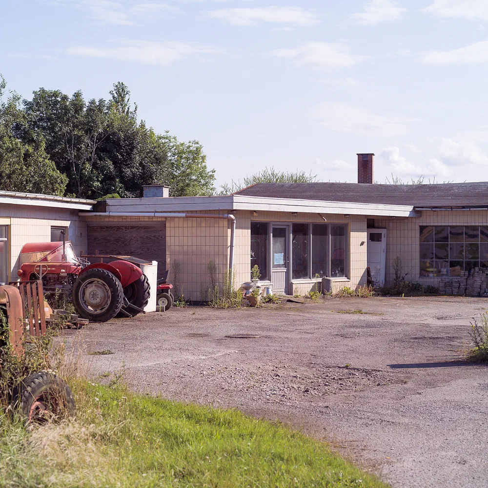 Old red tractor in front of a low tractor and car workshop in Fårevejle