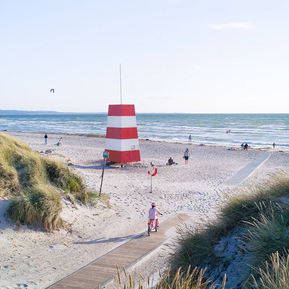 Red and white lifeguard tower on the sandy beach at Gudmindrup Strand with a child on a bike on the boardwalk