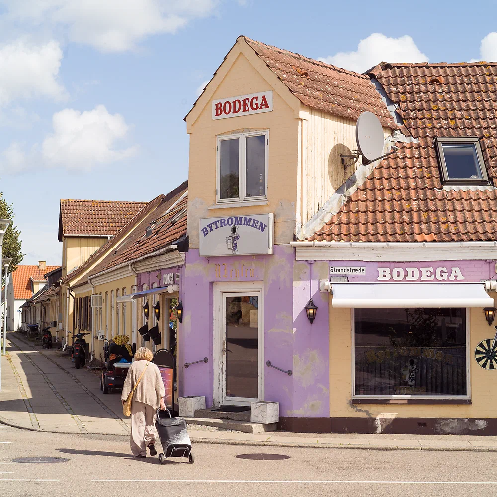 Woman with a shopping trolley walking past the purple Bodega Bytrommen in Nykøbing Sjælland
