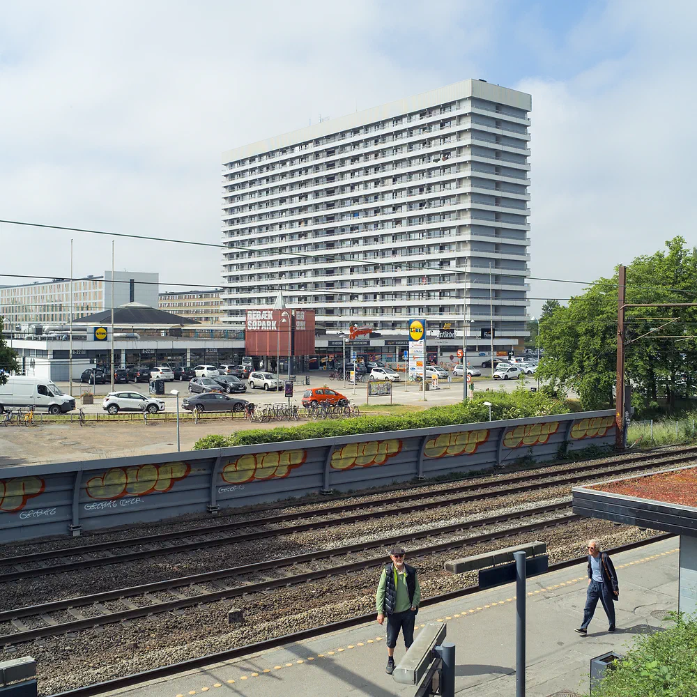 Railway tracks in front of the tall white Rebæk Søpark apartment tower in Hvidovre