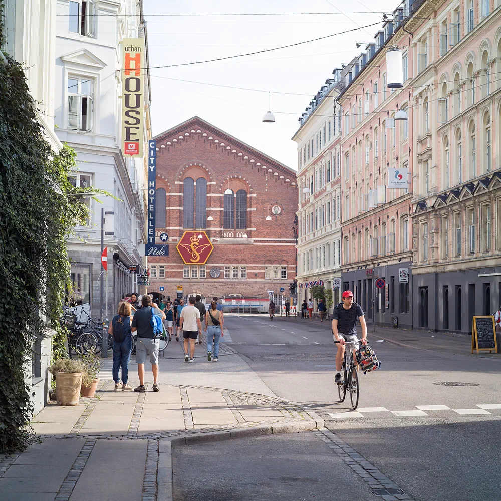 People walking and a cyclist on Istedgade with a red brick church at the end of the street