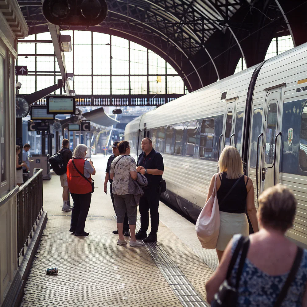 Passengers on a platform beside a train under the arched roof of Copenhagen Central Station