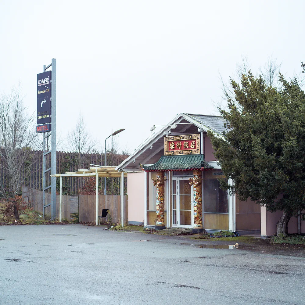 Abandoned Motel Oasen building with a Chinese restaurant sign by an empty wet road in Roskilde