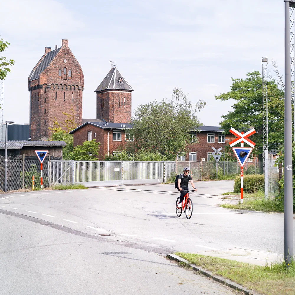 Old red brick railway buildings and a level crossing with a cyclist in South Copenhagen