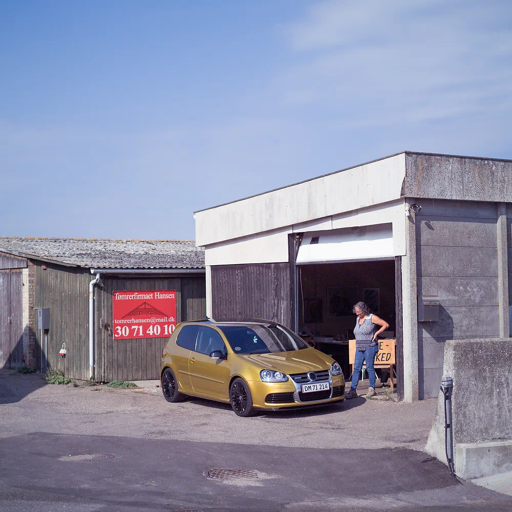 Woman standing by a gold Volkswagen Golf outside an open concrete garage in Havnebyen