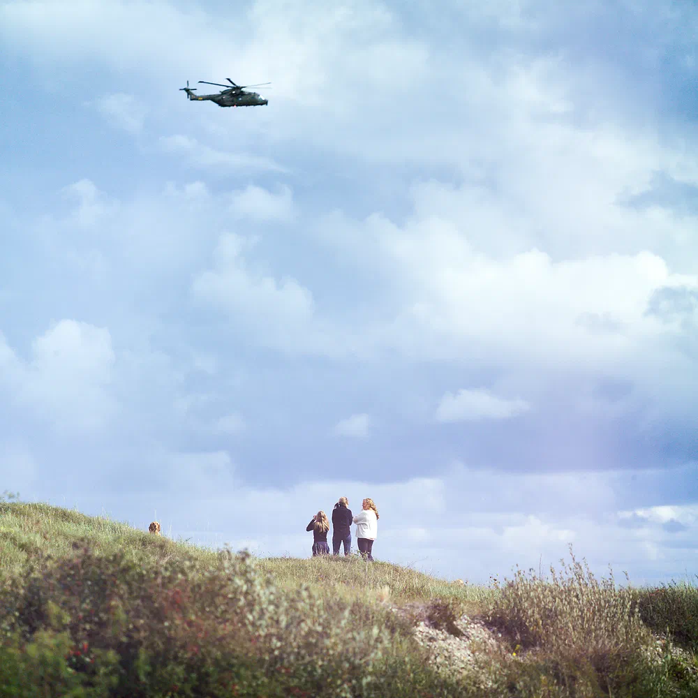 Search and rescue helicopter flying over three people standing on a grassy dune at Sjællands Odde