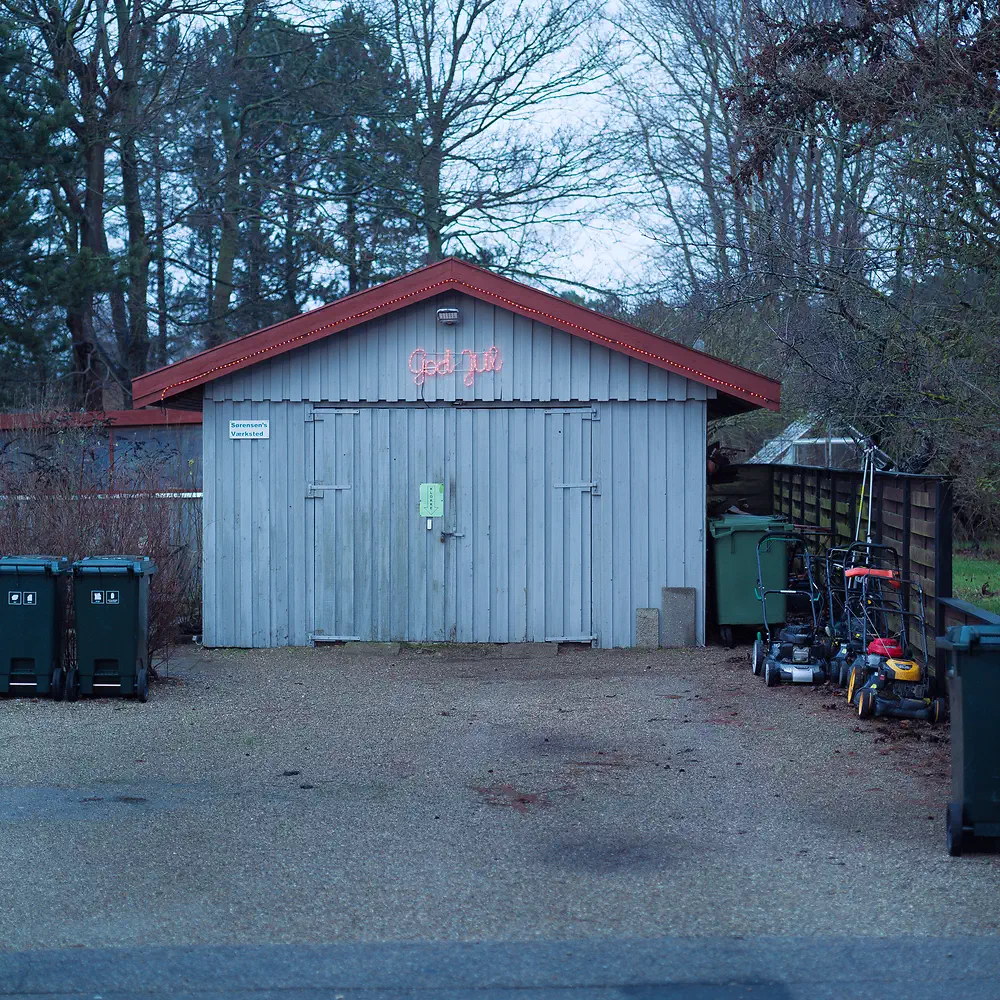 Grey garden shed with God jul written on it, bins and lawnmowers in winter