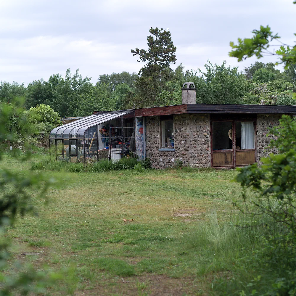 Old stone summer house with a glass conservatory behind tall grass