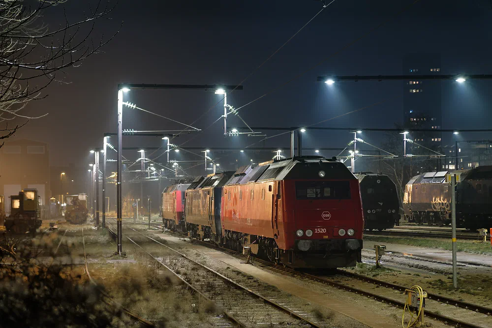 Red DSB locomotives in a train yard at night under bright floodlights