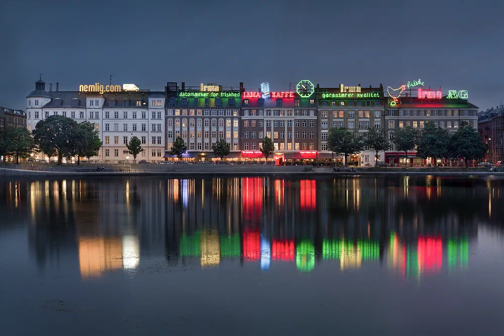 Neon signs on the buildings along the Lakes in Copenhagen reflected in the water at dusk