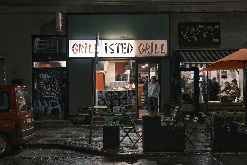 Isted Grill on Istedgade at night with its illuminated sign and a woman standing in the doorway
