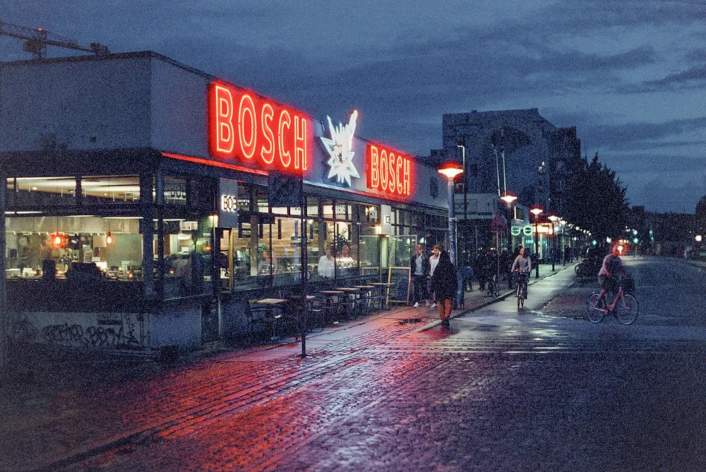 Red Bosch neon sign on a building in Kødbyen, Copenhagen, reflected in the wet cobblestones at dusk