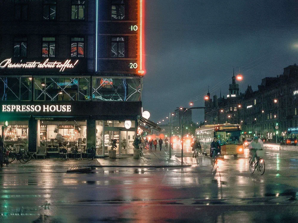Neon signs and Espresso House on a rainy evening at Rådhuspladsen in Copenhagen with cyclists and a bus